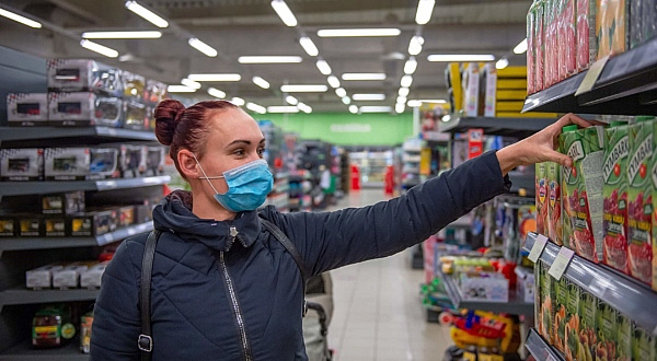 Eine Frau mit Einwegmaske greift in einem Supermarkt in ein Regal.